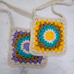 Two Granny Square Bags layered on a marble background. With yarn colors of yellow, purple, cream and caramel.