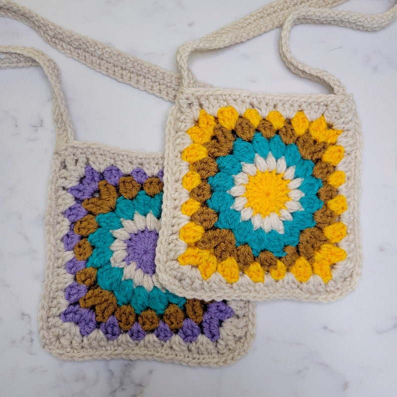 Two Granny Square Bags layered on a marble background. With yarn colors of yellow, purple, cream and caramel.