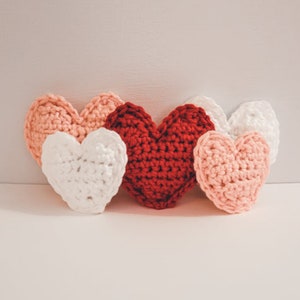 A set of small and large crochet hearts made of bulky yarn against a white backdrop. There are two pink, two white and one red heart.