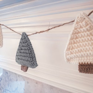 Crocheted Christmas Trees strung into a garland draped across a white mantle with jute. The trees are made of green and cream yarn with light brown trunks.