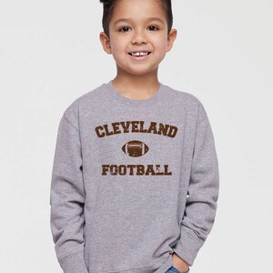 May include: A grey long-sleeved sweatshirt with a brown vintage-style graphic that says "CLEVELAND FOOTBALL" with a football graphic.
