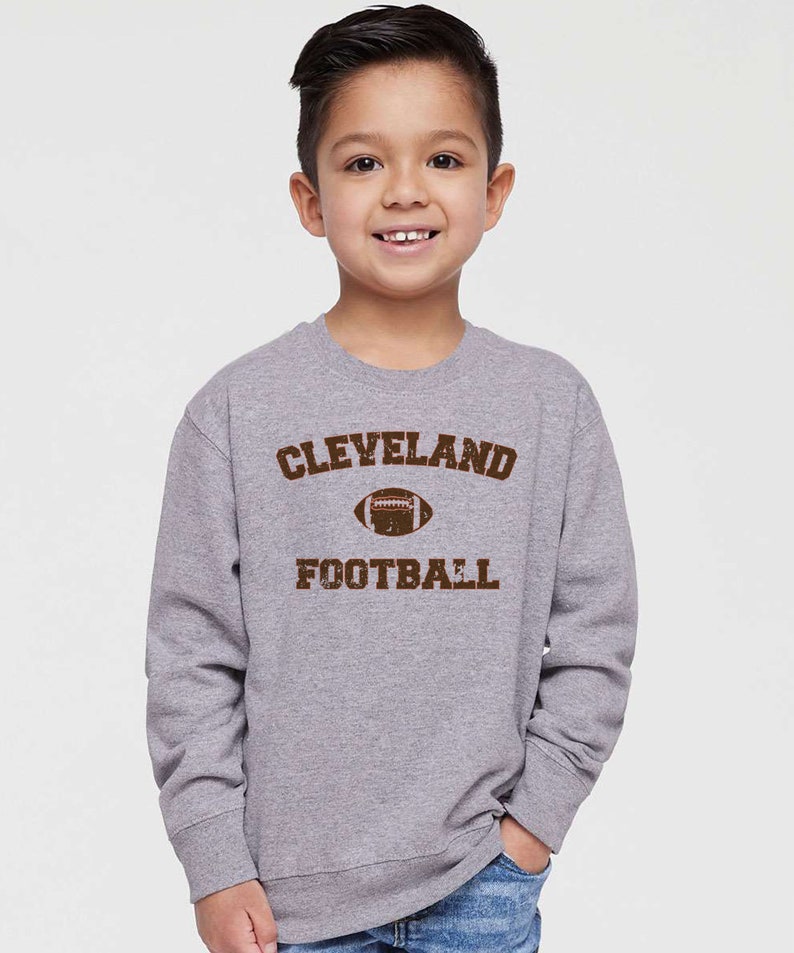 May include: A grey long-sleeved sweatshirt with a brown vintage-style graphic that says "CLEVELAND FOOTBALL" with a football graphic.