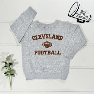 May include: Grey sweatshirt with a brown vintage-style graphic that says "CLEVELAND FOOTBALL" with a football graphic in the centre.