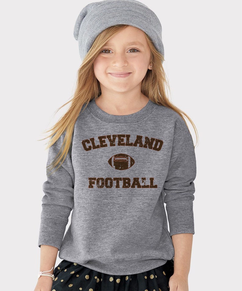 May include: Grey long-sleeved sweatshirt with brown text that reads "CLEVELAND FOOTBALL" and a brown football graphic.