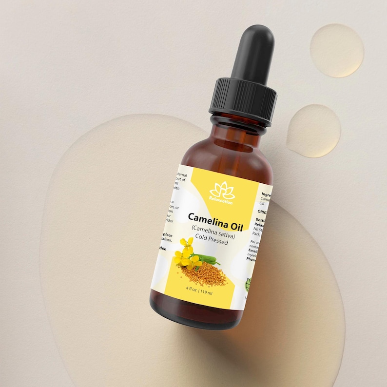 Peut inclure: Une bouteille en verre brun d'huile de cam&eacute;line avec un compte-gouttes noir. L'&eacute;tiquette porte le texte "Camelina Oil (Camelina sativa) Cold Pressed" et une illustration de fleurs jaunes et de graines. La bouteille contient 119 ml.