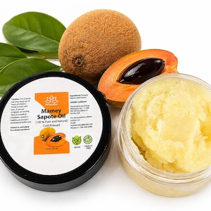 Pode incluir: Um recipiente preto redondo de óleo de sapoti com um rótulo branco com detalhes em laranja e texto, ao lado de um pote transparente aberto contendo uma substância semissólida amarelo-pálida, um sapoti inteiro, um fruto cortado e folhas verdes.