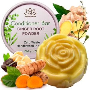 Op de afbeelding: Een gele conditionerbar in de vorm van een roos met een label waarop staat "Relaxcation Conditioner Bar Ginger Root Powder Zero Waste Handcrafted in [onleesbaar] 2oz / 57g". De bar is omringd door gemberwortel, kurkumawortel en groene bladeren.