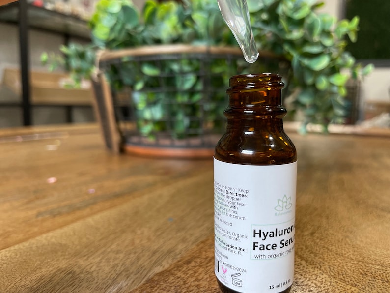 May include: A brown glass bottle with a dropper filled with a clear liquid. The bottle is labeled "Hyaluronic Face Serum with organic rose oil" and "15 ml (0.5 fl oz)".