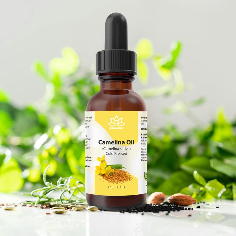 Peut inclure: Une bouteille en verre brun d'huile de cam&eacute;line avec un compte-gouttes noir. L'&eacute;tiquette jaune indique "Camelina Oil (Camelina sativa) Cold Pressed". La bouteille contient 119 ml. Le fond pr&eacute;sente du feuillage vert et des graines.