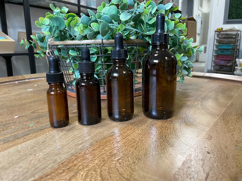 May include: Four amber glass bottles with black dropper tops of varying sizes. The bottles are arranged in a row on a wooden surface.