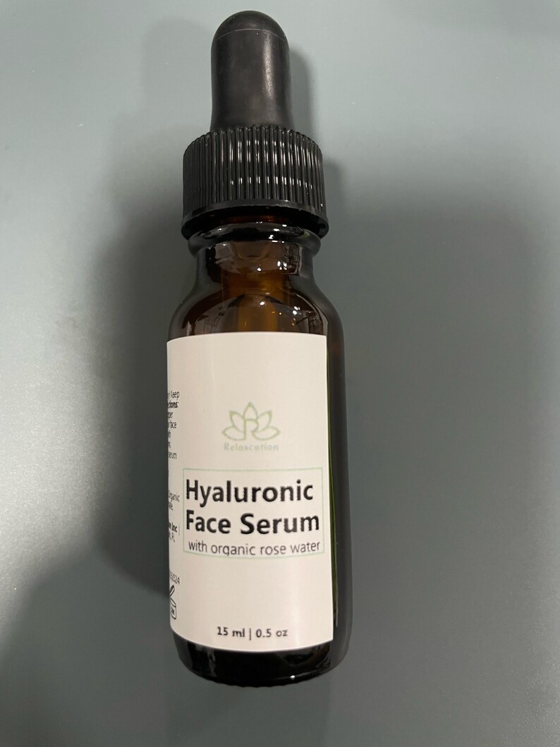 May include: A brown glass bottle with a black dropper top. The bottle is labeled "Hyaluronic Face Serum with organic rose water" and "15 ml | 0.5 oz".
