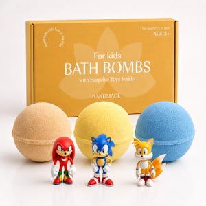 Puede incluir: Un conjunto de tres bombas de baño coloridas con juguetes sorpresa en el interior, con una caja que dice "For kids BATH BOMBS with Surprise Toys Inside HANDMADE". Las bombas de baño son de color beige, amarillo y azul. Los juguetes son personajes de Sonic the Hedgehog.