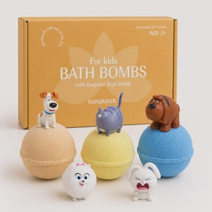 May include: A selection of children's bath bombs, each with a toy figurine on top. The bath bombs are in tan, yellow, and blue. The box in the background reads "For kids BATH BOMBS with Surprise Toys Inside". Each bath bomb weighs 142 grams.
