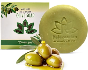 May include: A round green olive oil soap bar with the words "Relaxzation Handmade in the USA" printed on it. The soap is sitting on a white surface with a small pile of green olives and olive oil.
