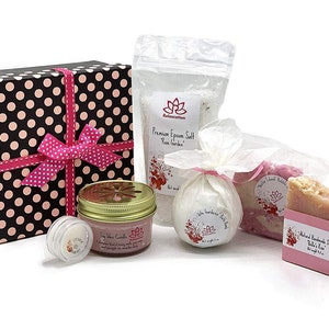 May include: A gift box set with a pink and black polka dot pattern, containing a soy wax candle, bath bomb, soap, and Epsom salt. The products are all scented with rose garden.