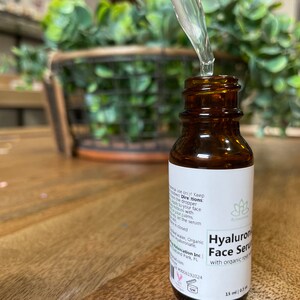 May include: A brown glass bottle with a white label that reads "Hyaluronic Face Serum with organic rose hip oil". The bottle is being filled with a clear liquid from a dropper.