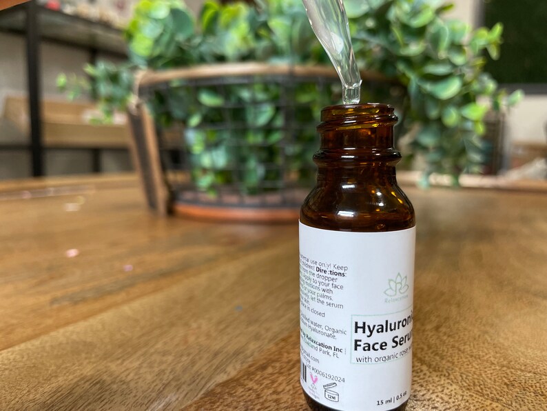 May include: A brown glass bottle with a white label that reads "Hyaluronic Face Serum with organic rose hip oil". The bottle is being filled with a clear liquid from a dropper.
