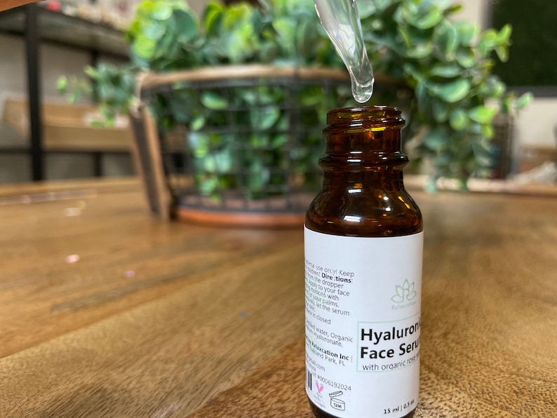 May include: A brown glass bottle with a white label that reads "Hyaluronic Face Serum with organic rosehip oil" and a dropper with a clear liquid. The bottle is sitting on a wooden surface.