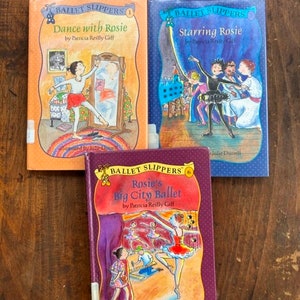 May include: Three children's books from the "Ballet Slippers" series. The covers feature illustrations of young ballerinas in various dance poses. Titles include "Dance with Rosie," "Starring Rosie," and "Rosie's Big City Ballet."
