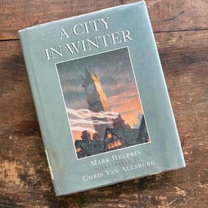 May include: A hardcover book titled "A City in Winter" with a dust jacket. The cover features a winter scene with a clock tower and falling snow. The author is Mark Helprin, illustrated by Chris Van Allsburg.