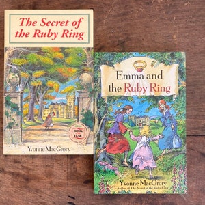 May include: Two paperback books with colorful covers featuring illustrations of a castle and a group of women walking in a garden. The books are titled "The Secret of the Ruby Ring" and "Emma and the Ruby Ring". Both books are by Yvonne MacGrory.