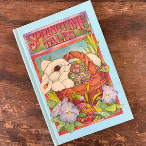 May include: A light blue book titled "Springtime Tales" with a bunny peeking out of a basket filled with colorful eggs and flowers. The cover features a vibrant illustration with a red border and purple pansies.