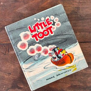 May include: Vintage children's book titled "Little Toot" with a colorful illustration of a tugboat. The cover features the title in red letters with a cartoon tugboat on the water. The author's name, Hardie Gramatky, is printed at the bottom.