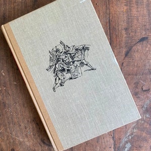 May include: A beige book with a black and white illustration of two figures on the cover. The figures are in a fighting pose, with one figure holding a sword and the other figure holding a shield.
