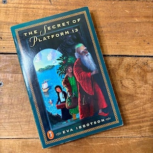May include: A hardcover book titled "The Secret of Platform 13" by Eva Ibbotson. The cover features a teal border and a colorful illustration of characters and a landscape scene. The Penguin logo is visible.