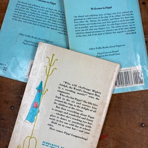 May include: A vintage children's book cover featuring a cartoon illustration of a girl with red hair and a blue dress standing on a stool. The text on the cover reads "Who will challenge Mighty Adolph, the World's Strongest Man, in a wrestling match?"  The book is published by Scholastic Book Services.