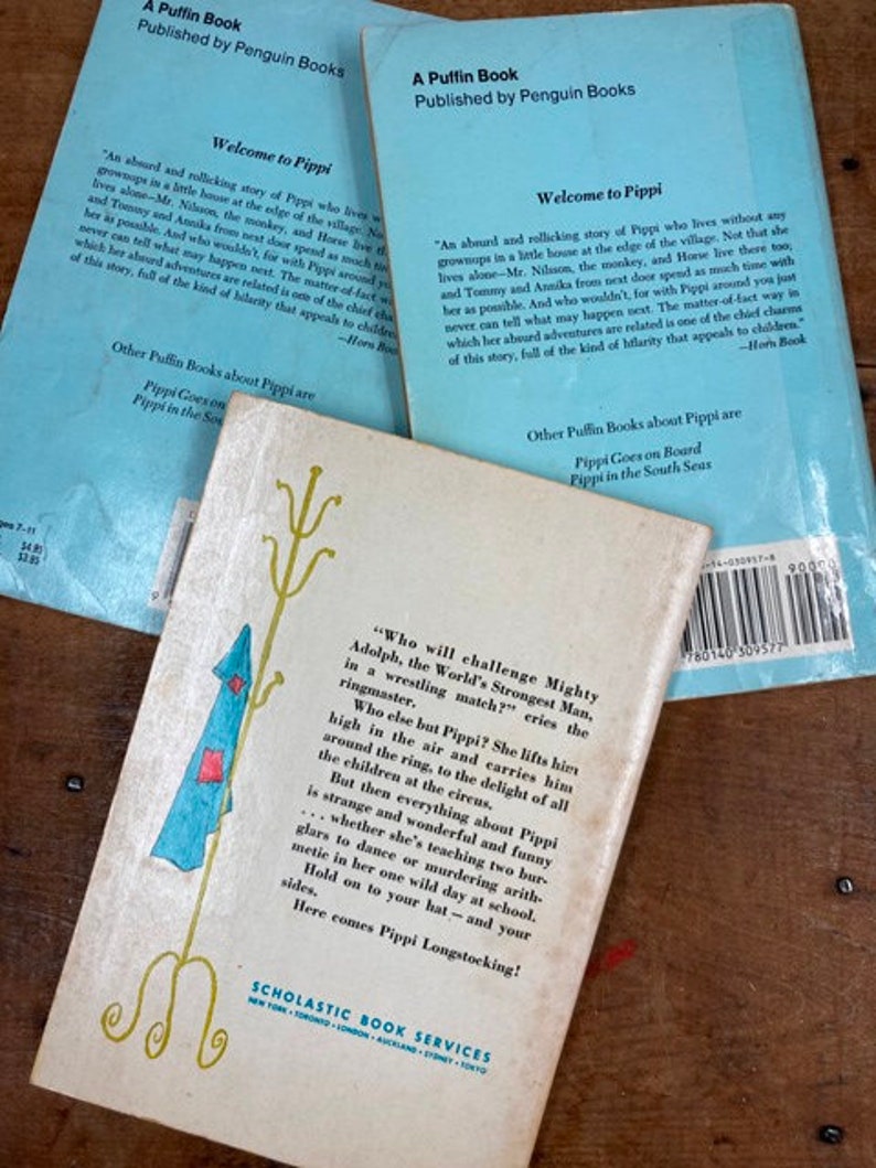 May include: A vintage children's book cover featuring a cartoon illustration of a girl with red hair and a blue dress standing on a stool. The text on the cover reads "Who will challenge Mighty Adolph, the World's Strongest Man, in a wrestling match?"  The book is published by Scholastic Book Services.