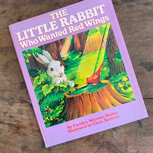 May include: A children's book titled "The Little Rabbit Who Wanted Red Wings" with a purple cover. The cover illustration features a white rabbit, a red bird, and a forest scene. The book is by Carolyn Sherwin Bailey, illustrated by Chris Santoro.