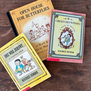 May include: Three vintage children's books with colorful covers are arranged on a wooden surface. The titles include "Open House for Butterflies," "Chicken Soup with Rice," and "One Was Johnny." The books feature illustrations and text, showcasing classic children's literature.
