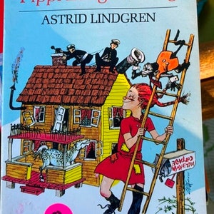 May include: A vintage children's book cover featuring a red-haired girl climbing a ladder with a horse in the background. The book title is "Pippi Longstocking" by Astrid Lindgren. The cover is illustrated in a cartoon style with bright colors.