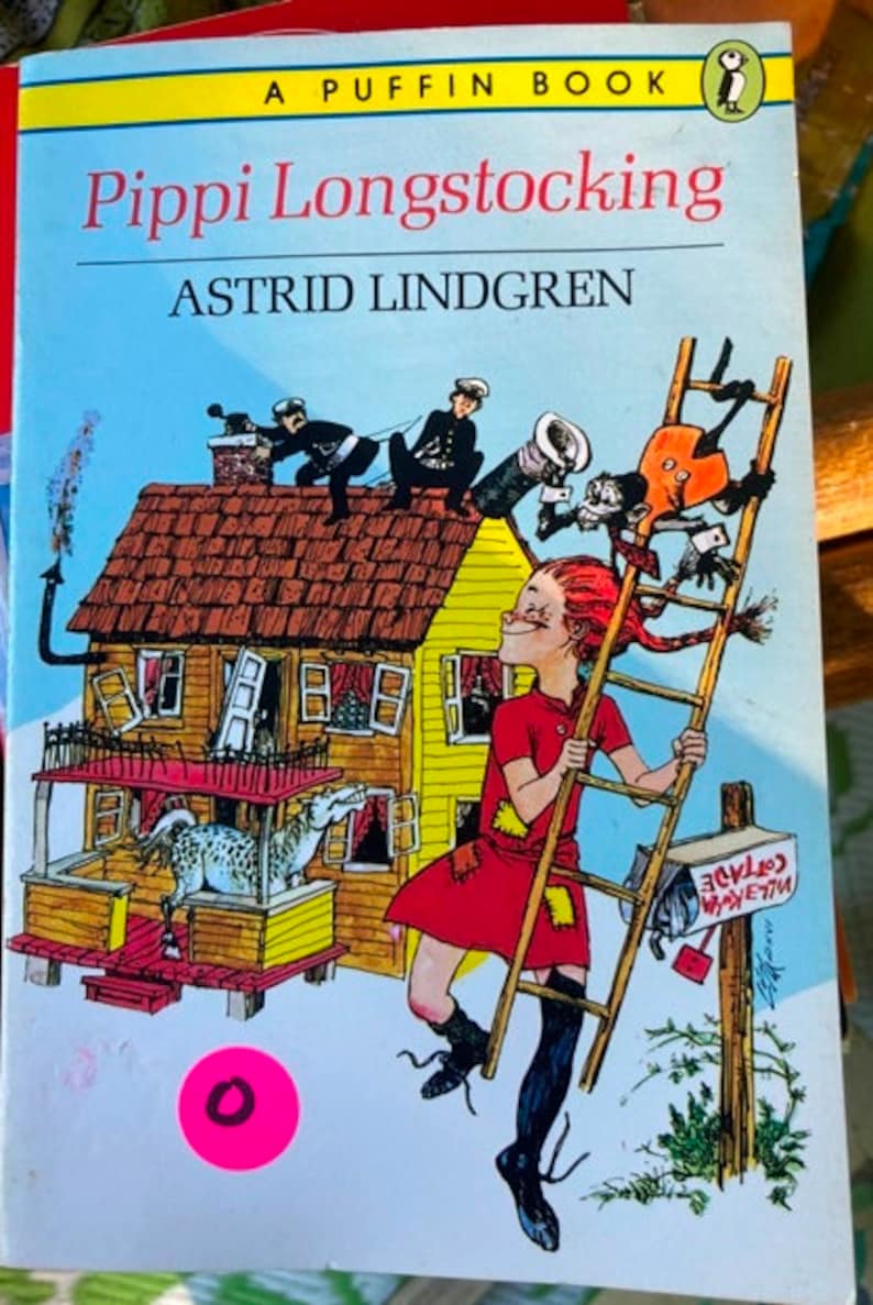 May include: A vintage children's book cover featuring a red-haired girl climbing a ladder with a horse in the background. The book title is "Pippi Longstocking" by Astrid Lindgren. The cover is illustrated in a cartoon style with bright colors.