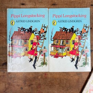 May include: Two identical paperback books titled "Pippi Longstocking" by Astrid Lindgren. The covers feature a cartoon illustration of a girl with red hair climbing a ladder on a yellow house.