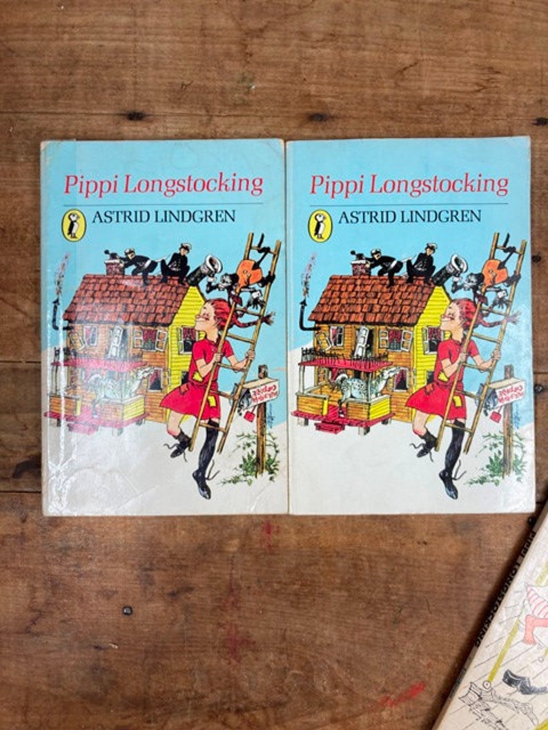 May include: Two identical paperback books titled "Pippi Longstocking" by Astrid Lindgren. The covers feature a cartoon illustration of a girl with red hair climbing a ladder on a yellow house.