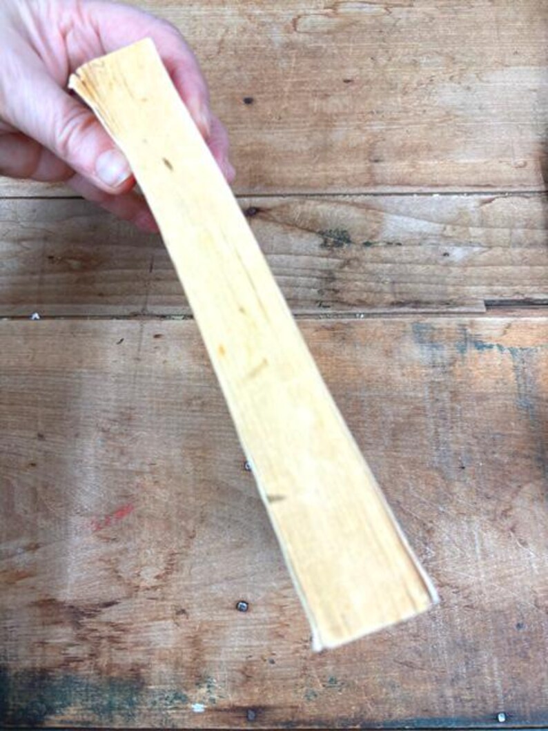 以下が含まれることがあります： 明るい色の長方形の木片を手に持っています。木材はわずかに粗い質感で、古くなっているように見えます。背景は素朴な外観の木製の表面です。