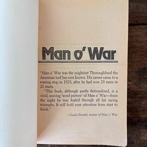以下が含まれることがあります： 太字の黒文字で「Man o' War」というタイトルが書かれた開いた本のページ。下のテキストは、馬のキャリアと本のコンテンツについて説明しています。ページは薄いタン色です。