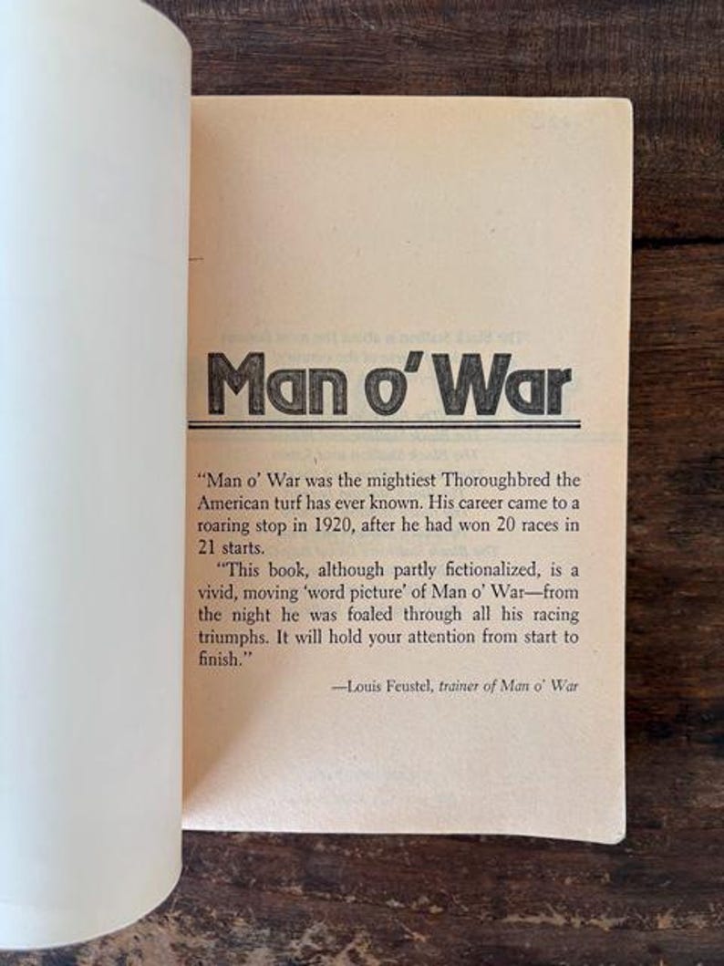 以下が含まれることがあります： 太字の黒文字で「Man o' War」というタイトルが書かれた開いた本のページ。下のテキストは、馬のキャリアと本のコンテンツについて説明しています。ページは薄いタン色です。