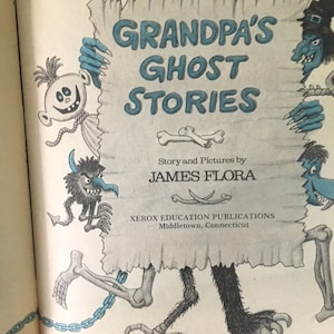 Pode incluir: Uma capa de livro com um monstro azul segurando um cartaz que diz "As hist&oacute;rias de fantasmas do av&ocirc;" com uma ilustra&ccedil;&atilde;o em preto e branco de um monstro no cartaz. O livro &eacute; de James Flora e publicado por Xerox Education Publications.
