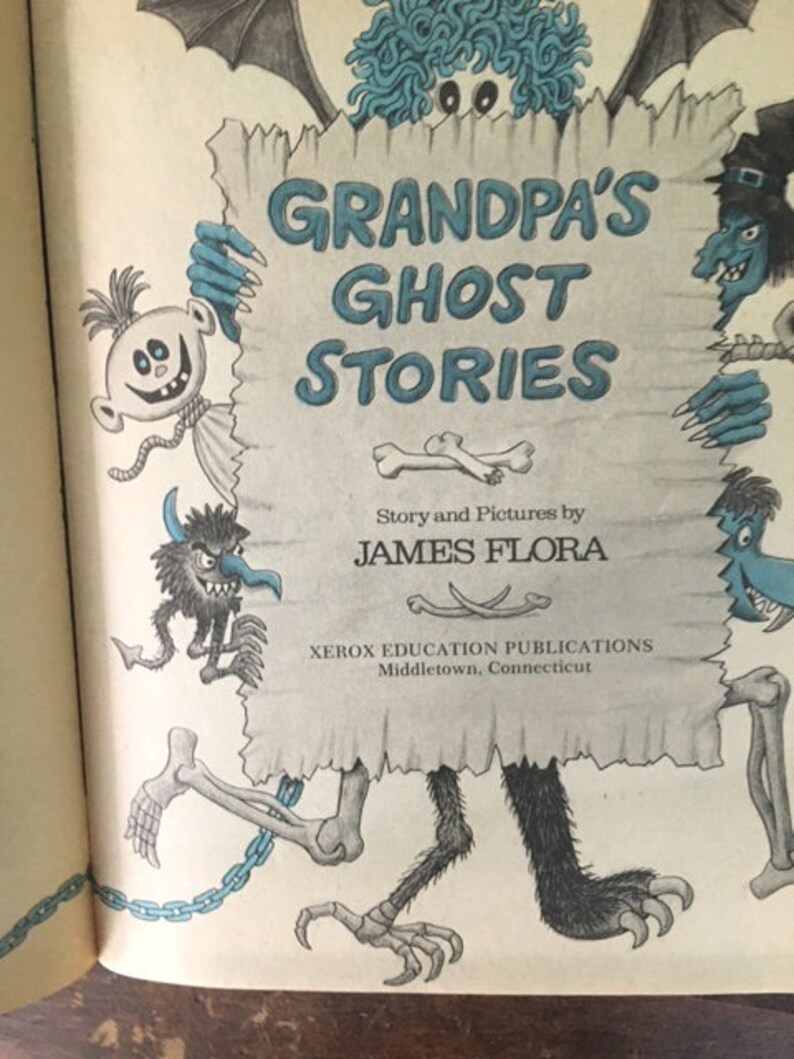 Pode incluir: Uma capa de livro com um monstro azul segurando um cartaz que diz "As hist&oacute;rias de fantasmas do av&ocirc;" com uma ilustra&ccedil;&atilde;o em preto e branco de um monstro no cartaz. O livro &eacute; de James Flora e publicado por Xerox Education Publications.