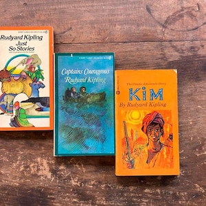 May include: Three vintage paperback books by Rudyard Kipling. The books are "Just So Stories", "Captains Courageous", and "Kim". The books have orange covers with illustrations.
