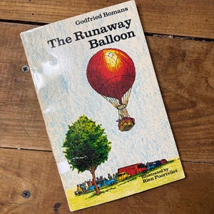 May include: A vintage copy of "The Runaway Balloon" by Godfried Bomans. The book cover features a red hot air balloon illustration against a light blue sky, with a green tree and vehicles below. Illustrated by Rien Poortvliet.