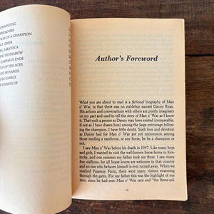 以下が含まれることがあります： 古紙に書かれたテキストが掲載された開いた本。右側のページには「Author's Foreword」と書かれており、Man o' Warの架空の伝記が詳しく書かれています。左側のページには、「Unwinding」や「Weakness」などの章のタイトルが記載されています。