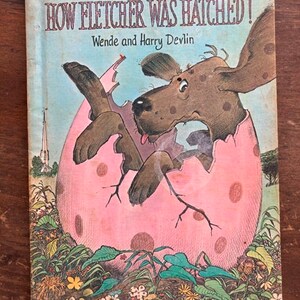 May include: A vintage children's book titled "How Fletcher Was Hatched!" by Wende and Harry Devlin. The cover features a cartoon illustration of a brown dog emerging from a pink egg with white polka dots.