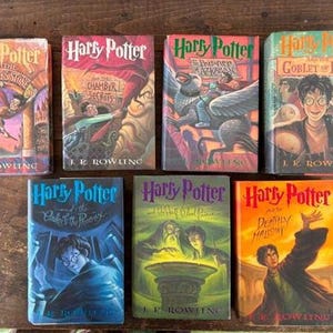 May include: A collection of seven Harry Potter books, each with unique cover art. The titles include "Harry Potter and the Sorcerer's Stone," "Chamber of Secrets," "Prisoner of Azkaban," "Goblet of Fire," "Order of the Phoenix," "Half-Blood Prince," and "Deathly Hallows."