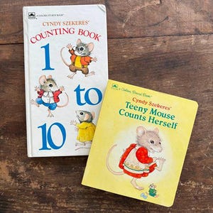 May include: Two children's books with mouse illustrations. One book is titled "Cyndy Szekeres' Counting Book 1 to 10" with a white cover and blue numbers. The other book is titled "Teeny Mouse Counts Herself" with a yellow cover.