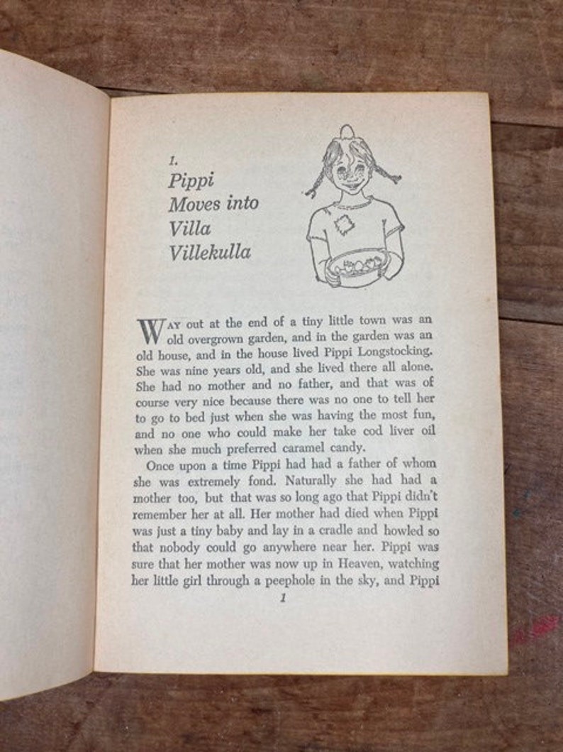 May include: A black and white illustration of a young girl with pigtails holding a bowl of fruit. The text "Pippi Moves into Villa Villekulla" is printed above the illustration. The text describes a young girl who lives alone in a house with an overgrown garden.