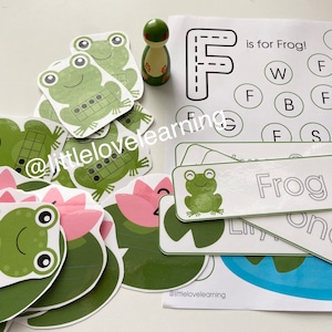 May include: A set of printable educational materials for preschoolers featuring a green frog, lily pads, and the letter F. The printable sheets include a letter tracing activity, a letter matching game, and a word building activity. The text on the sheets reads "F is for Frog!" and "Frog".